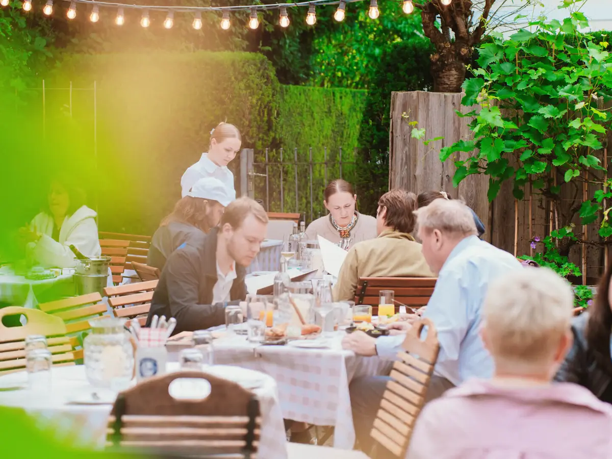 Kleines Jacob Personen sitzen an Holztischen im Biergarten der Weinwirtschaft Kleines Jacob.