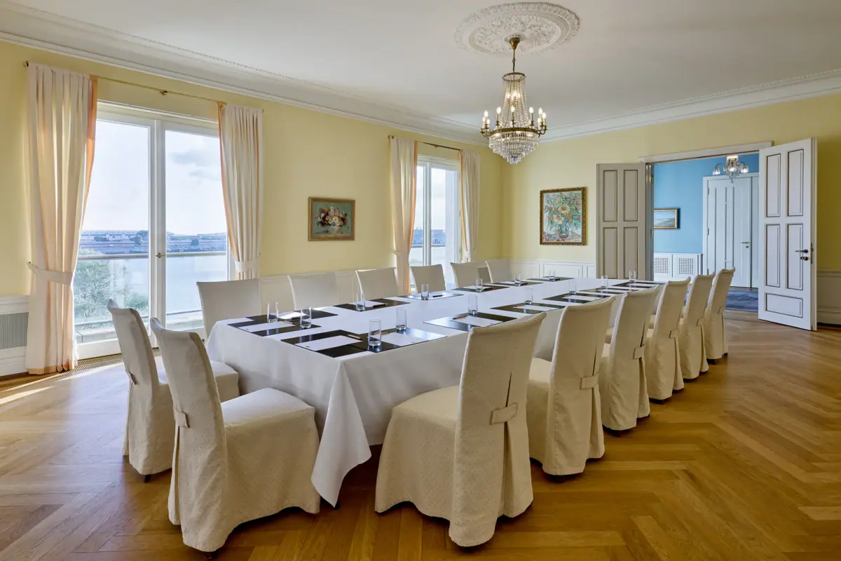 Ein großer Konferenzraum mit einem Tischblock, vielen Stühlen und großen Fenstern mit Elbblick.