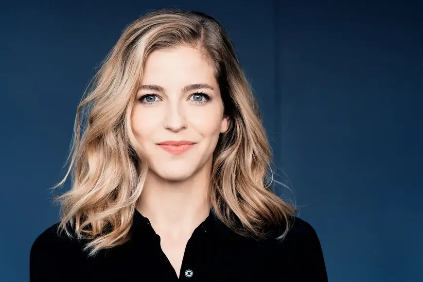 Karina Canellakis steht vor einem dunkelblauen Hintergrund und lächelt in die Kamera. 