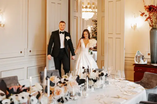 Hochzeitspaar frontal Hochzeitspaar stehet neben einem gedeckten Tisch in einem Innenraum