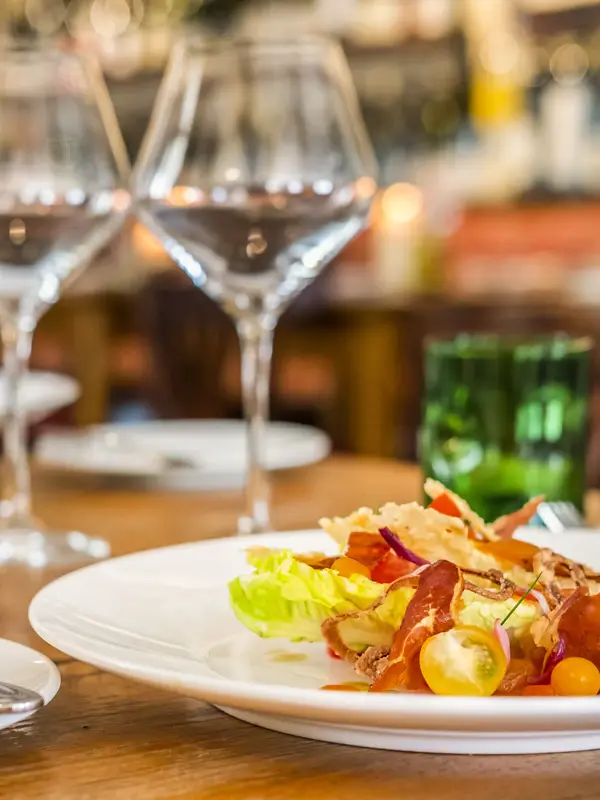 Gedeckter Tisch im Holzraum der Weinwirtschaft Kleines Jacob mit einem Teller mit Salat und Gläsern.