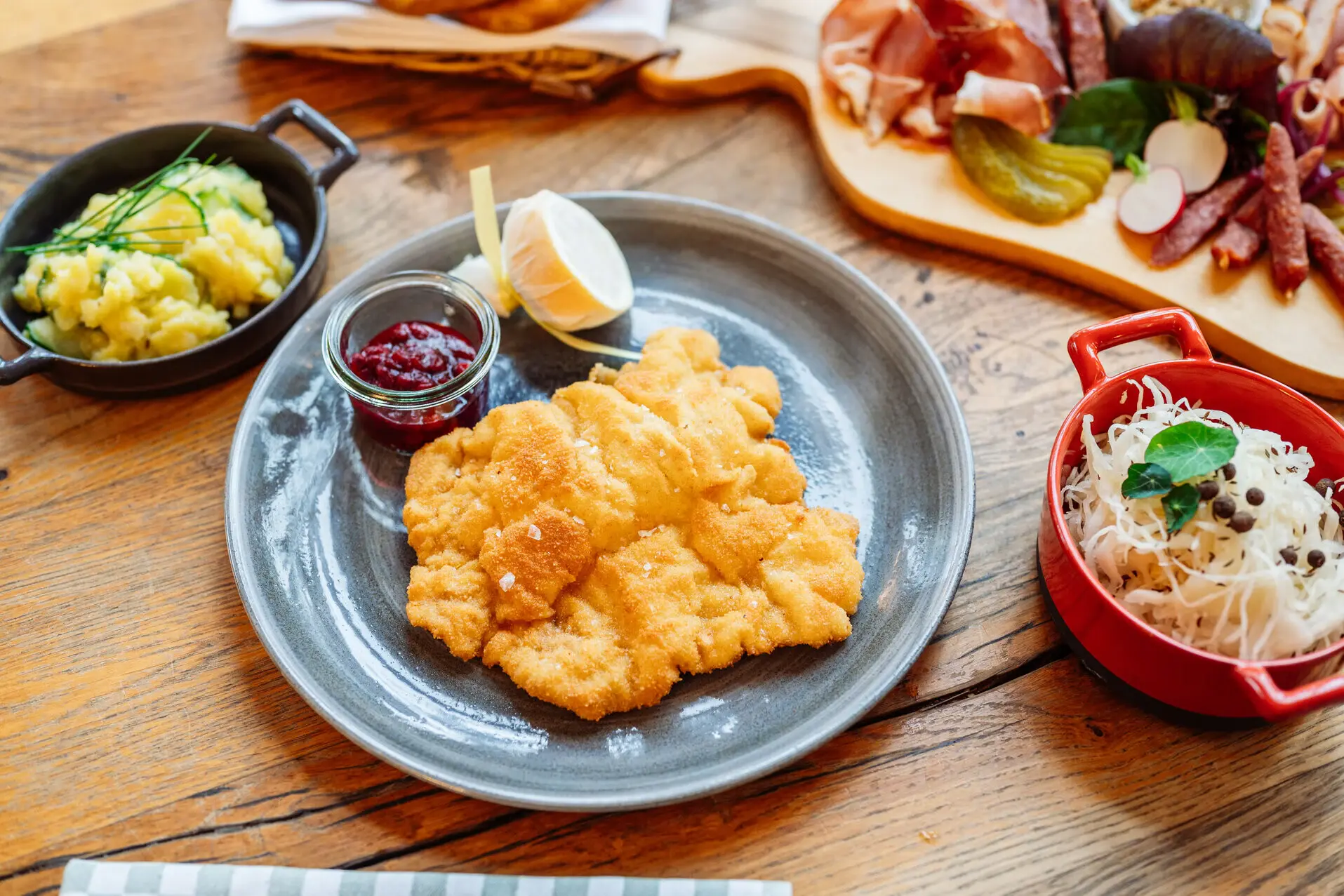 Ein Teller mit einem Schnitzel, Kartoffelsalat sowie eine Wurstplatte auf einem Tisch.
