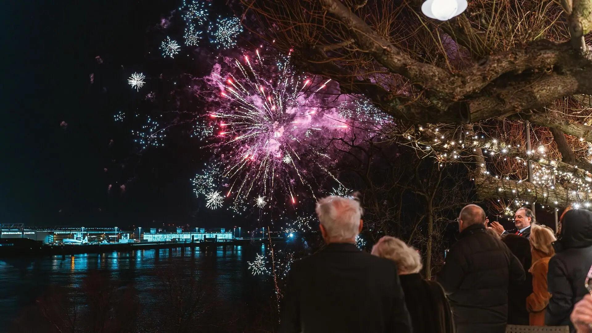 Eine Gruppe von Menschen betrachtet Feuerwerk an Silvester auf der Lindenterrasse vom Louis C. Jacob Hotel in Hamburg.