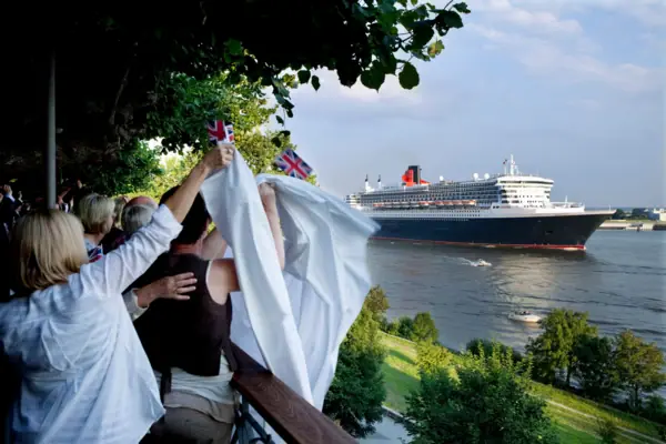 Eine Gruppe von Menschen hält Fahnen und winkt vor einem großen Schiff.